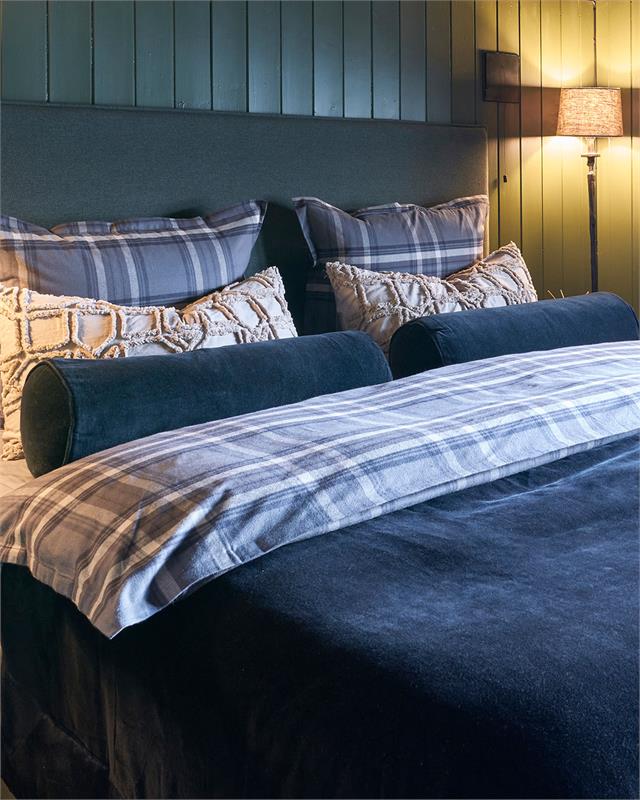 Seng ferdig oppredd i svart sengeteppe og rutene flanell sengetøy fra Halvor Bakke
