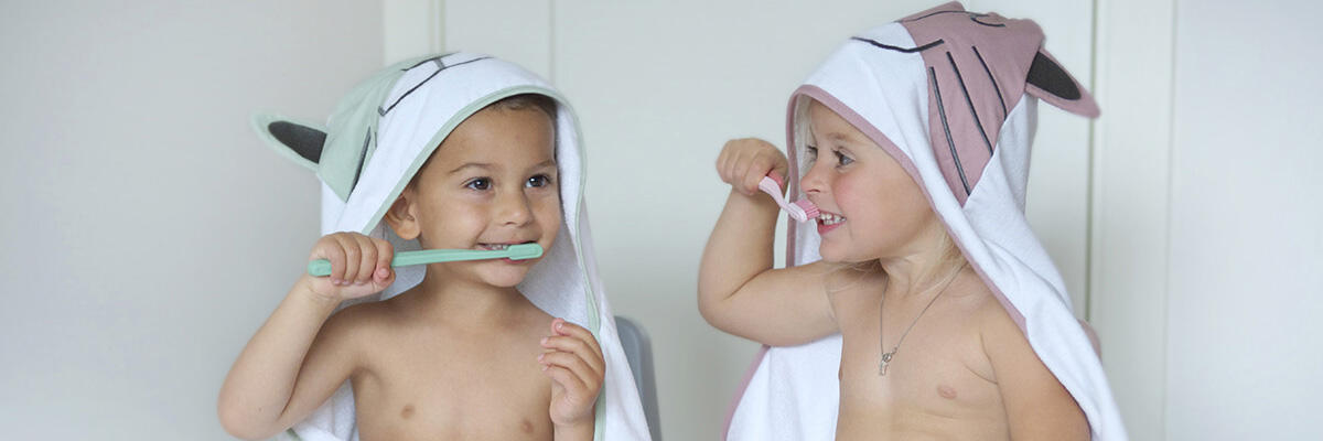 To gutter med hettehåndkle på seg og som pusser tenner. Bilde
