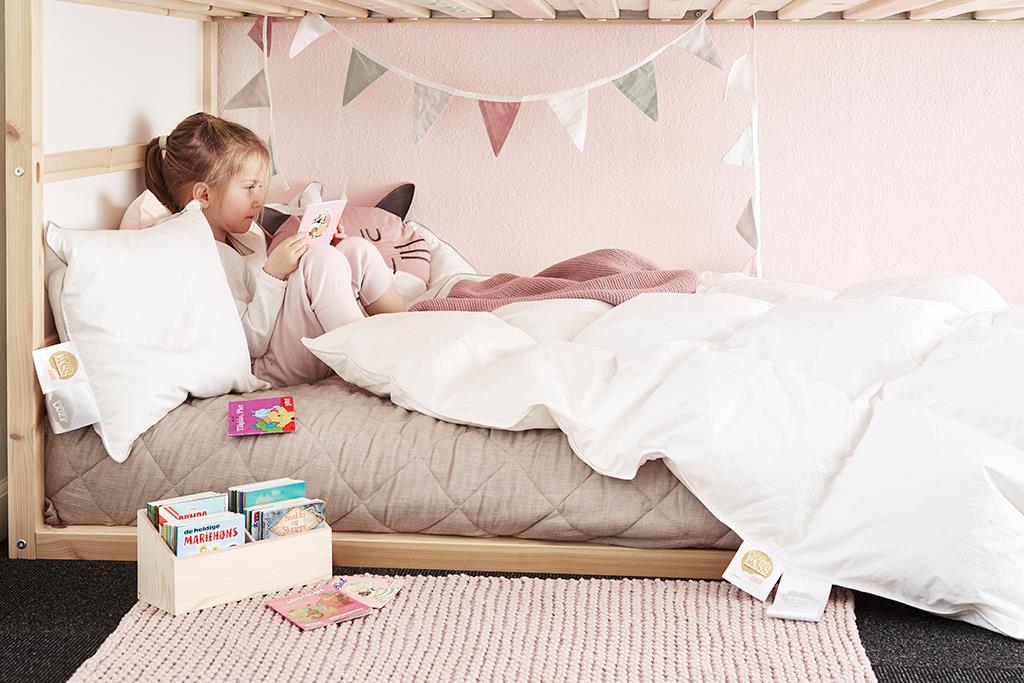 Jente som sitter i sengen og leser en bok. Dundyner og dunputer fra Norsk Dun. Bilde