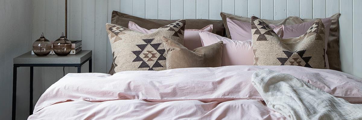 Seng ferdig oppredd i lyse farger med et sengeteppe i lin som ligger på kanten.